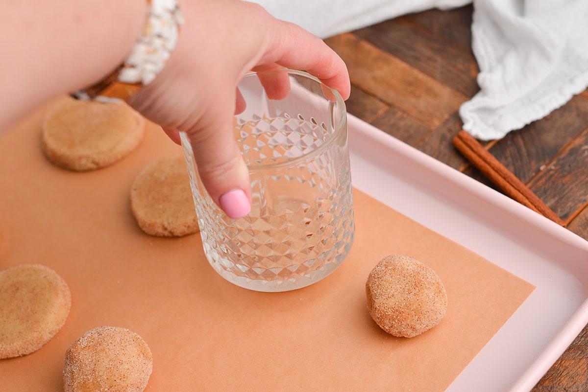 hand using glass to flatten cookie dough balls
