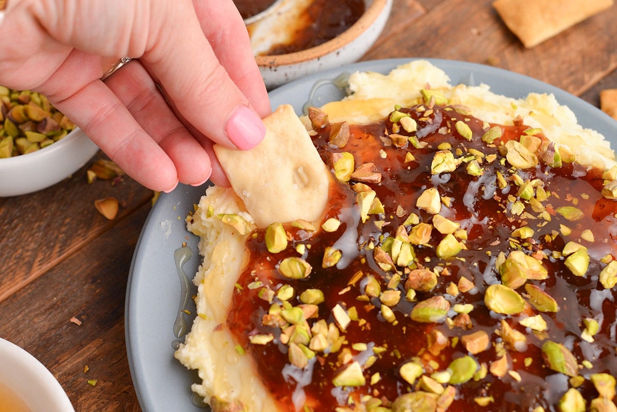 hand dipping cracker into brie dip