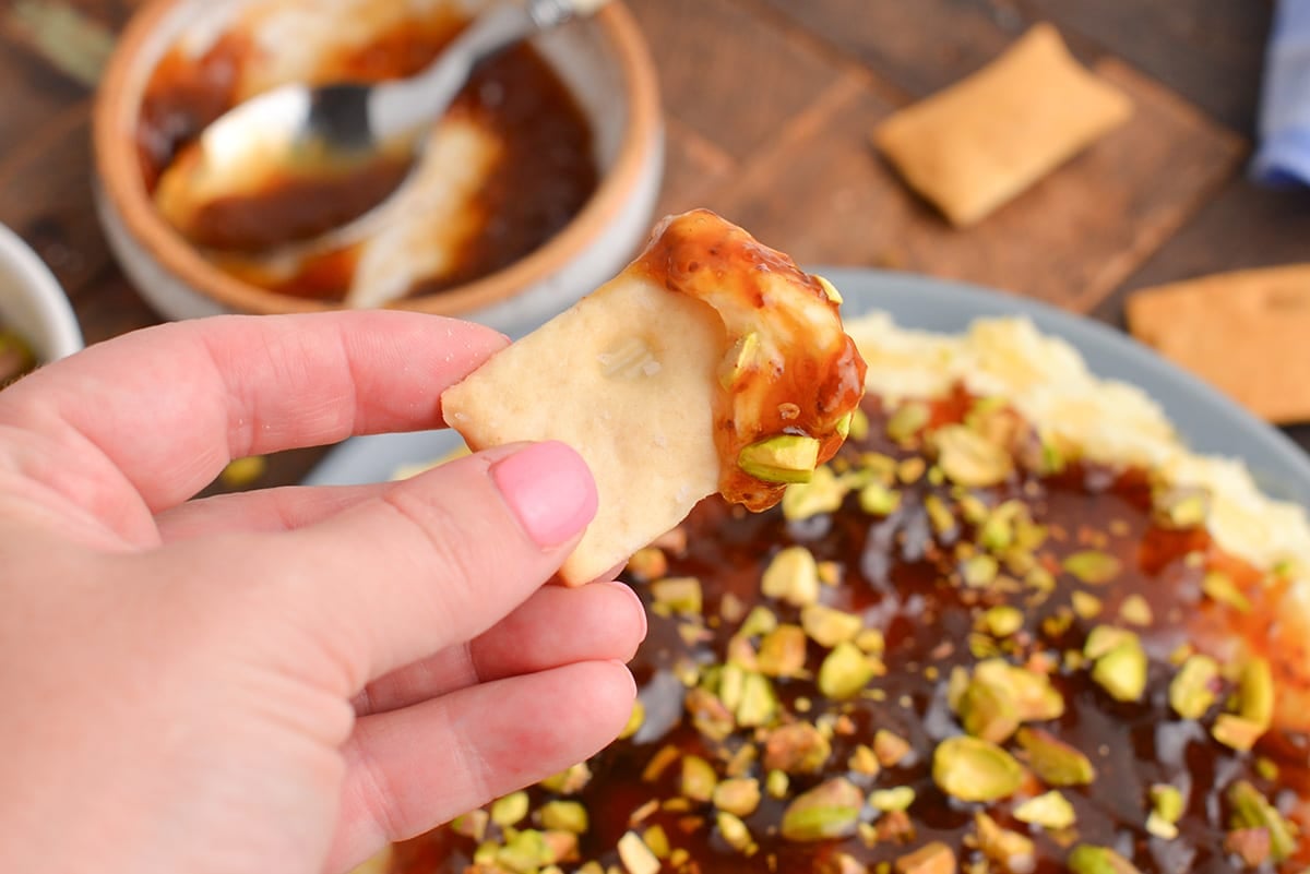 close up of hand holding cracker dipped into brie dip