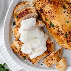 overhead shot sliced baked chicken breasts topped with sauce on a platter