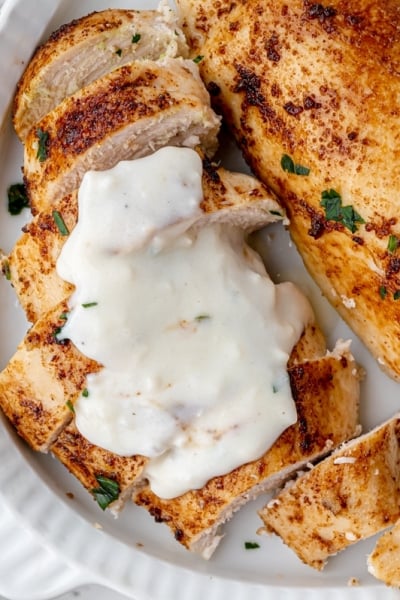 overhead shot sliced baked chicken breasts topped with sauce on a platter