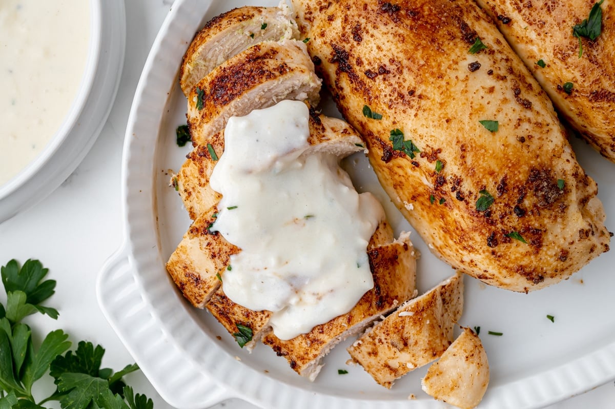 overhead shot sliced baked chicken breasts topped with sauce on a platter