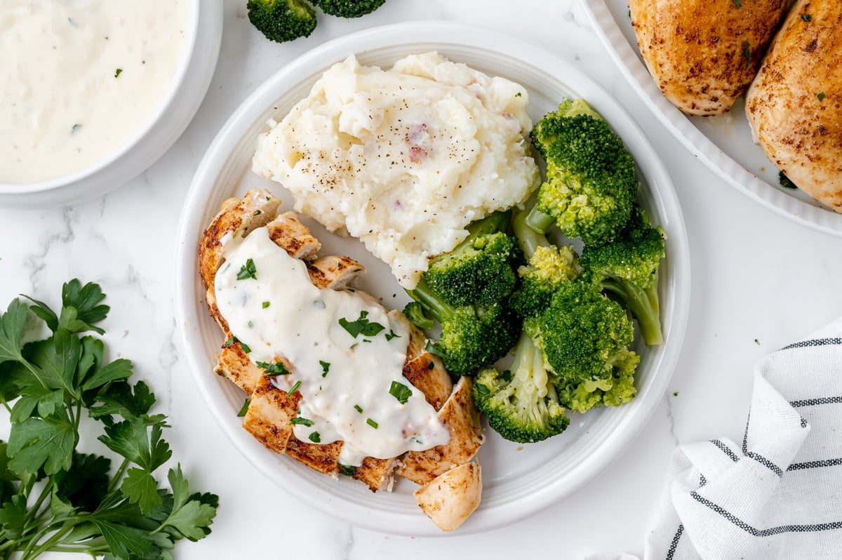 overhead shot of sliced baked chicken breast topped with sauce with potatoes and broccoli