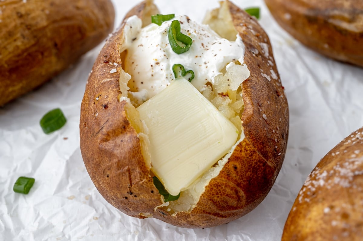 straight on shot of baked potato in oven topped with sour cream and butter