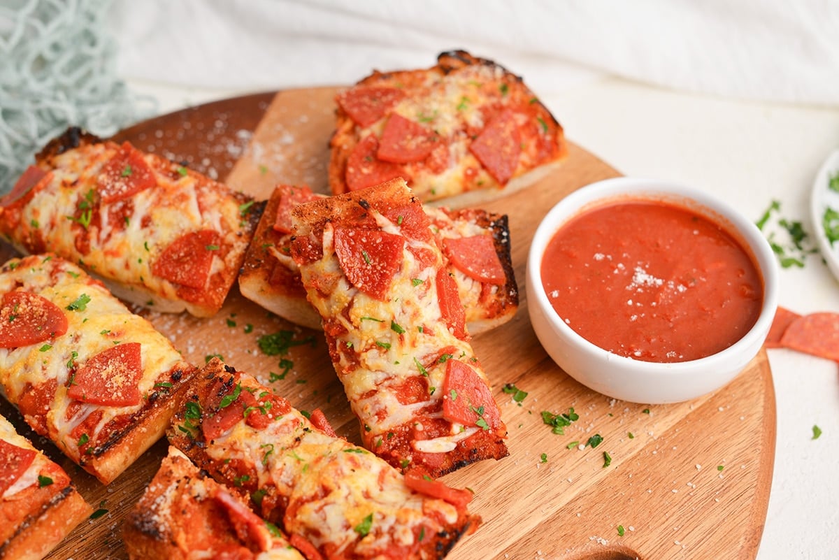 stacked slices of french bread pizza on board with bowl of sauce