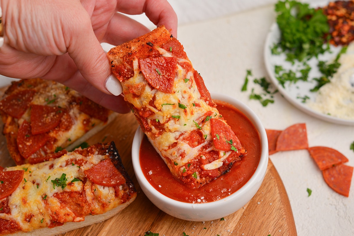 hand dipping slice of pizza into dipping sauce