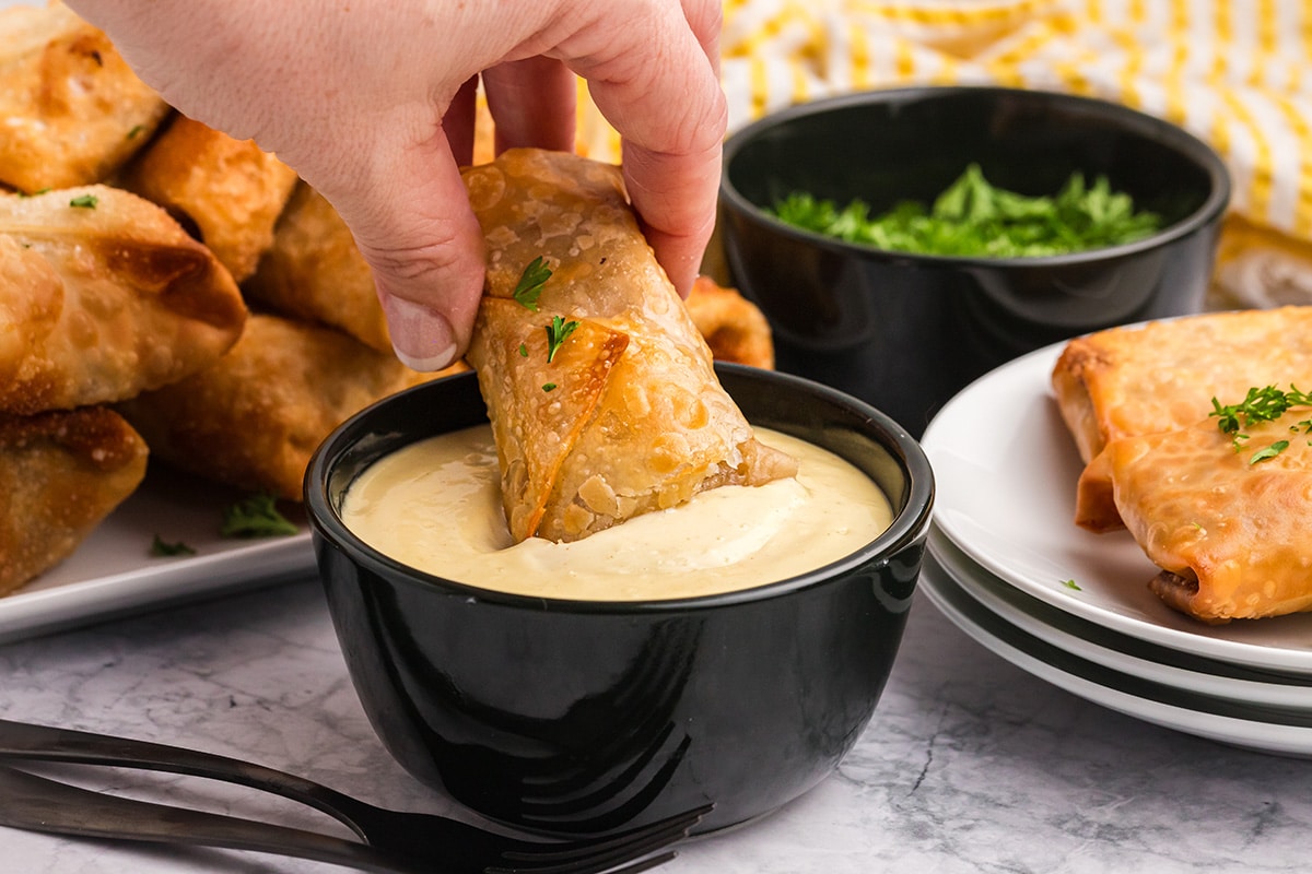 hand dipping german egg roll into bowl of sauce