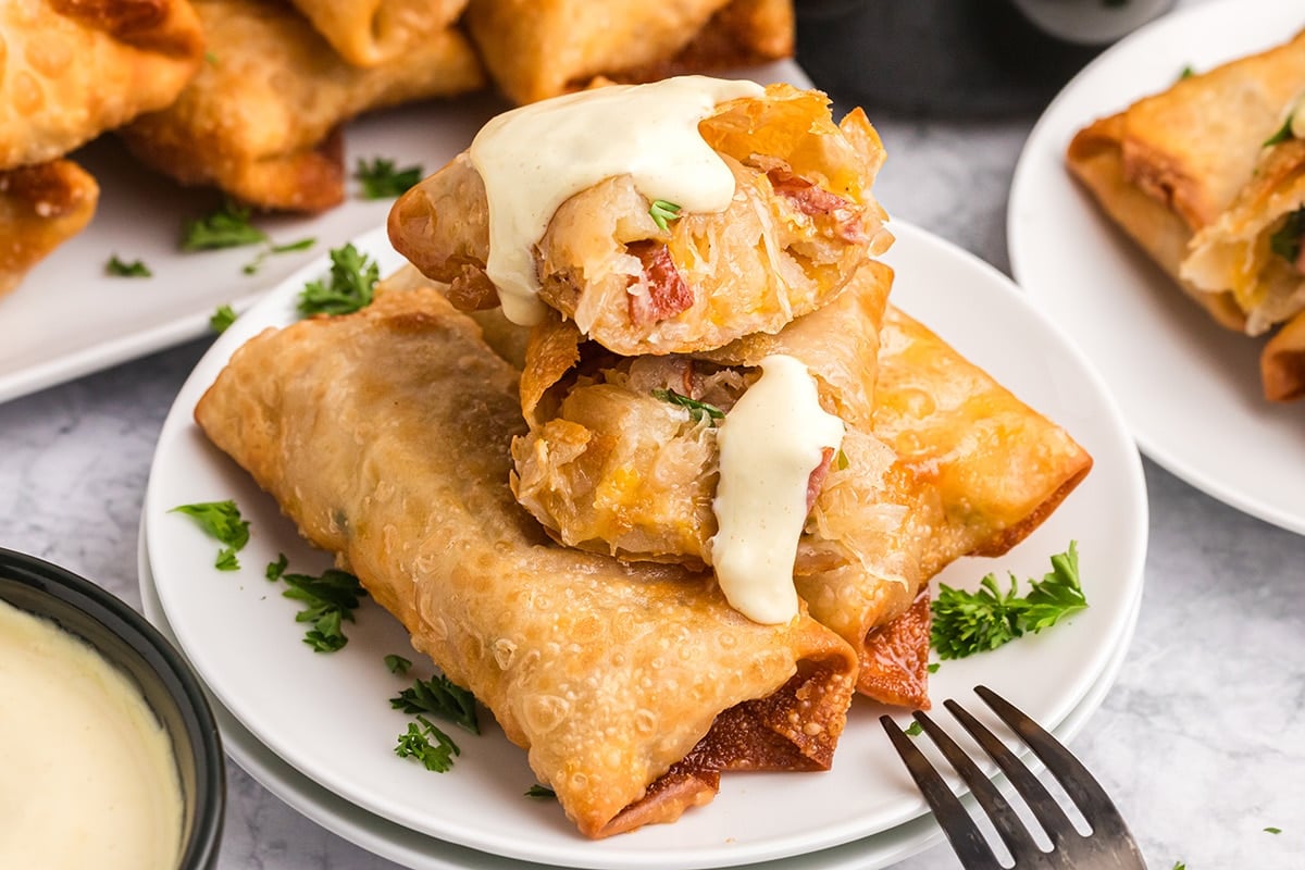 angled shot of pork and sauerkraut egg rolls on a plate topped with sauce