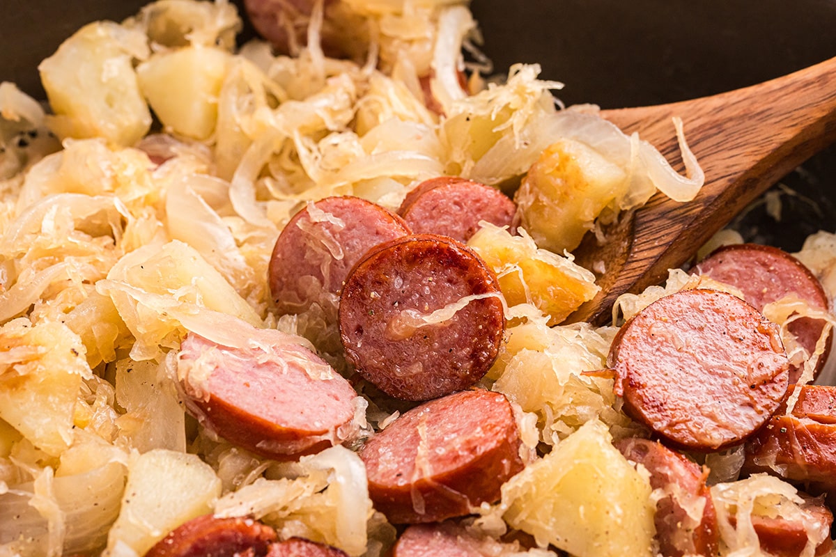 close up of wooden spoon in skillet of sauerkraut and pork