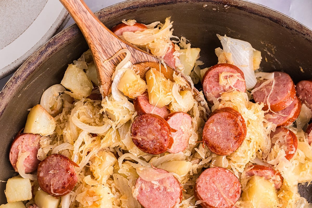 overhead shot of wooden spoon in skillet of sauerkraut and pork