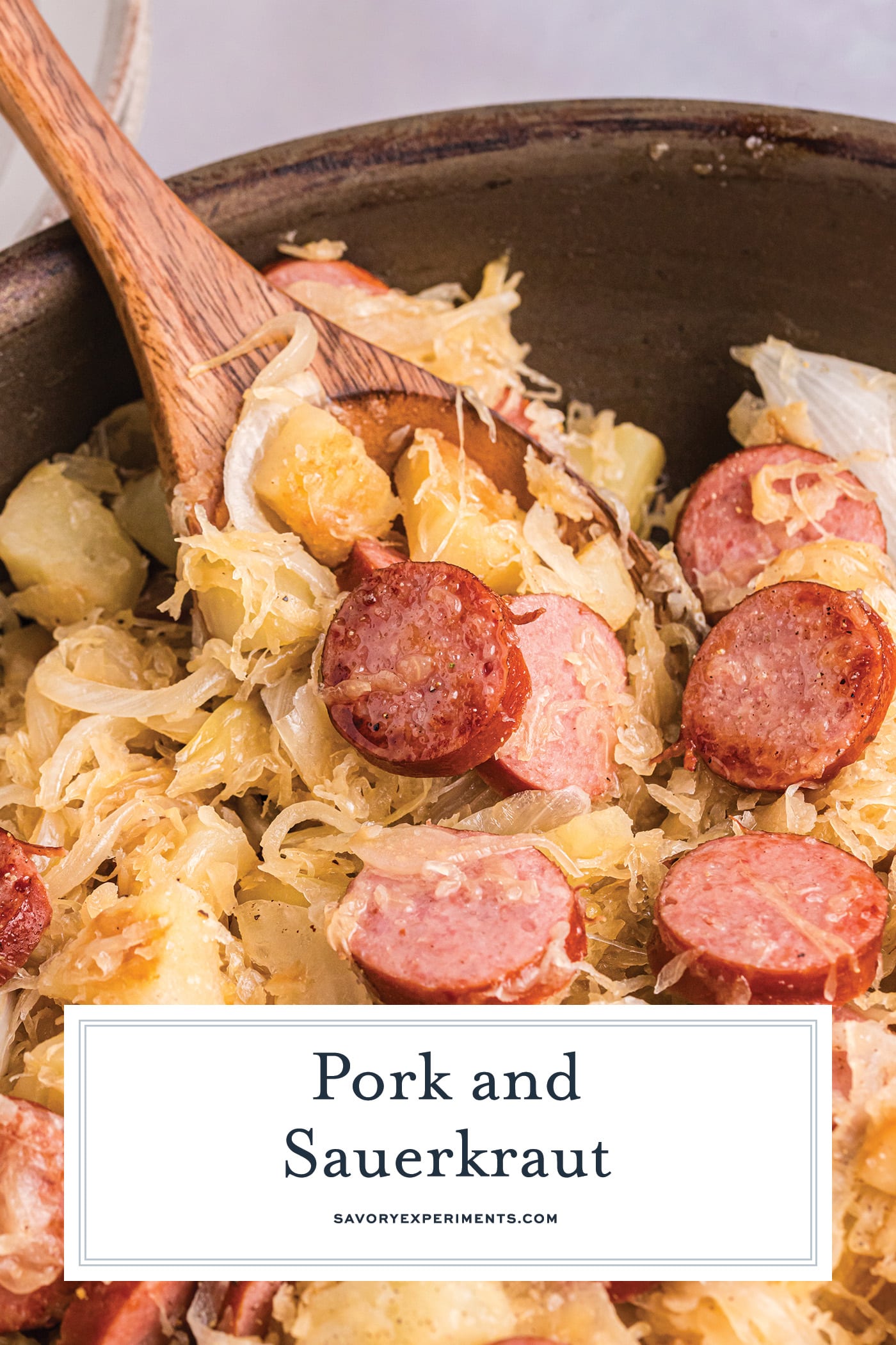 wooden spoon in skillet of pork and sauerkraut with text overlay for pinterest