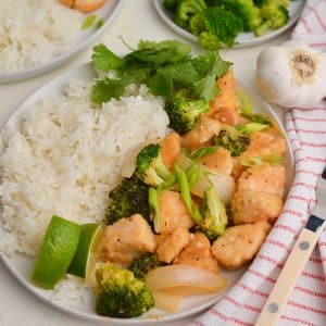 thai coconut chicken with white rice, limes and fresh cilantro on a white plate