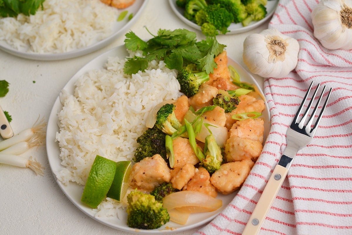 thai coconut chicken with white rice, limes and fresh cilantro on a white plate