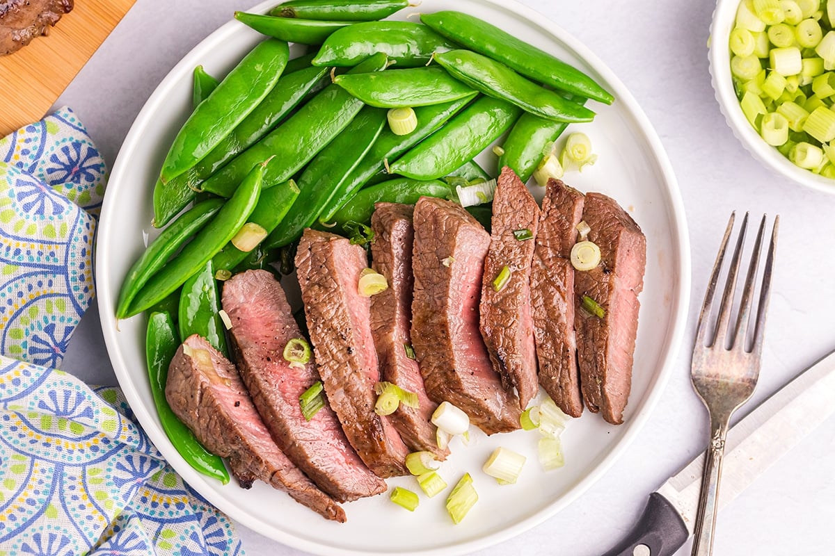overhead shot of plate of sliced steak with snap peas
