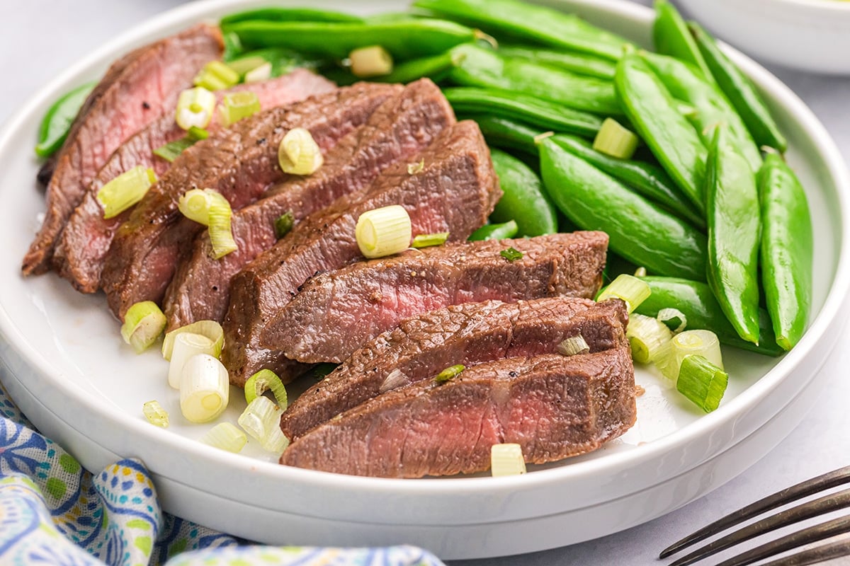 angled shot of sliced steak on plate with snap peas