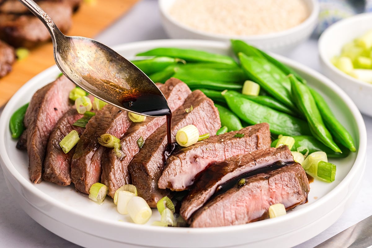 spoon pouring sauce over sliced steak