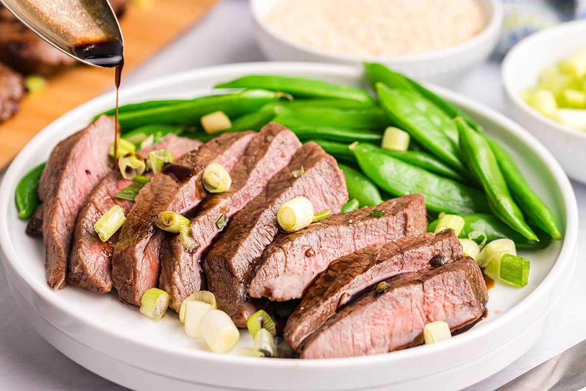 sauce poured over sliced asian steak on a plate with snap peas