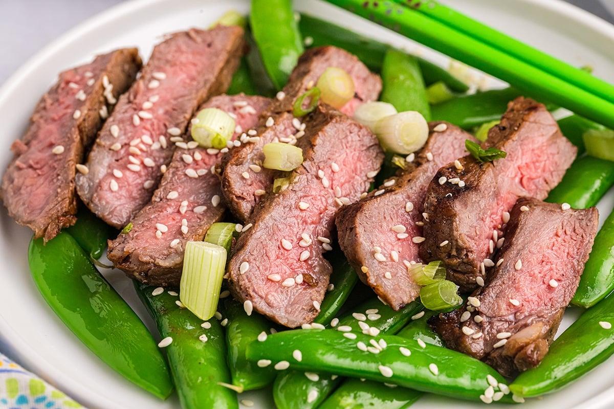 angled shot of sliced asian steak over bed of snap peas