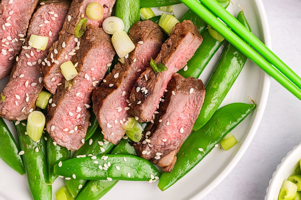 overhead shot of sliced asian steak over bed of snap peas