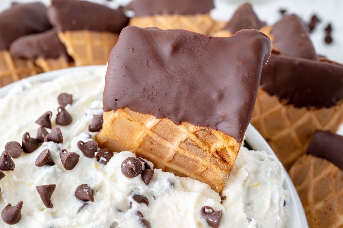 close up of chocolate dipped waffle cone piece in bowl of cannoli dip