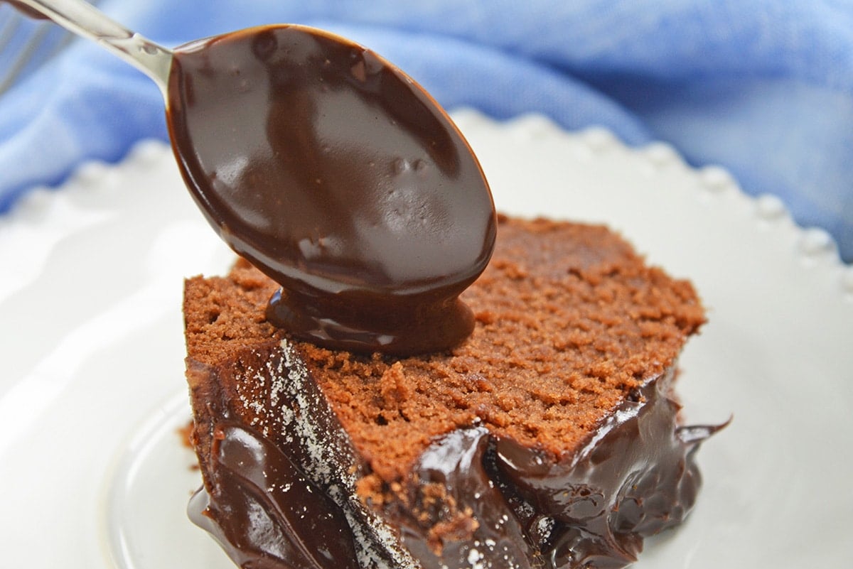 spooning chocolate sauce onto a piece of chocolate cake