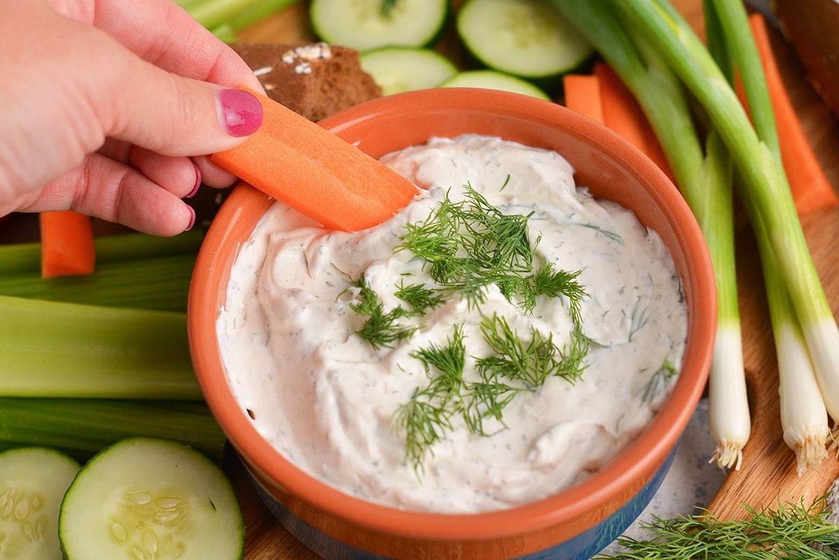 hand dipping carrot into bowl of dill dip