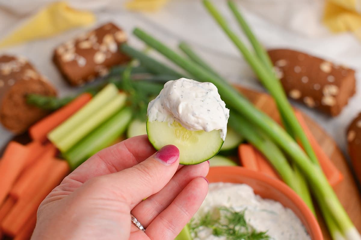 hand holding cucumber with dill dip on it