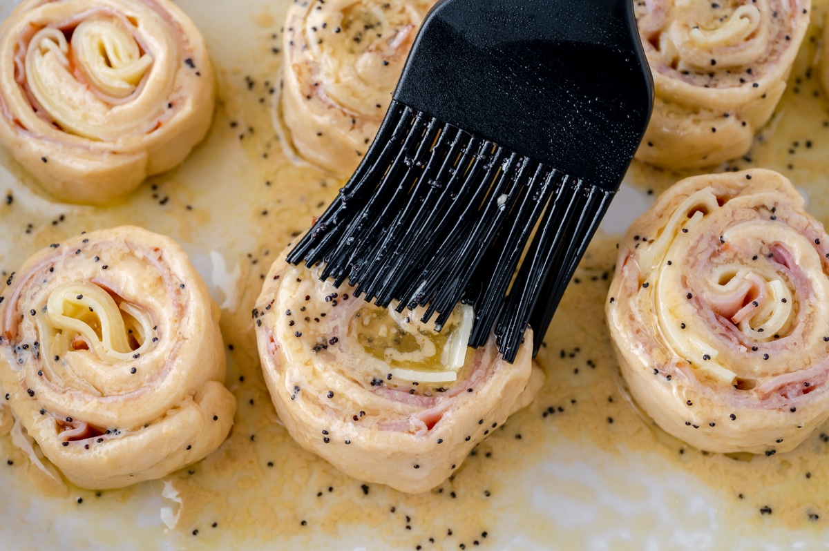 brushing poppy seed topping onto pinwheels