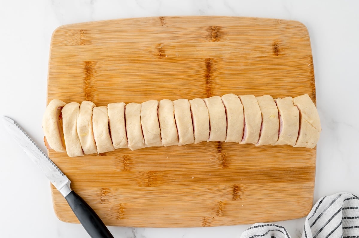 sliced rolled up crescent dough on cutting board with knife