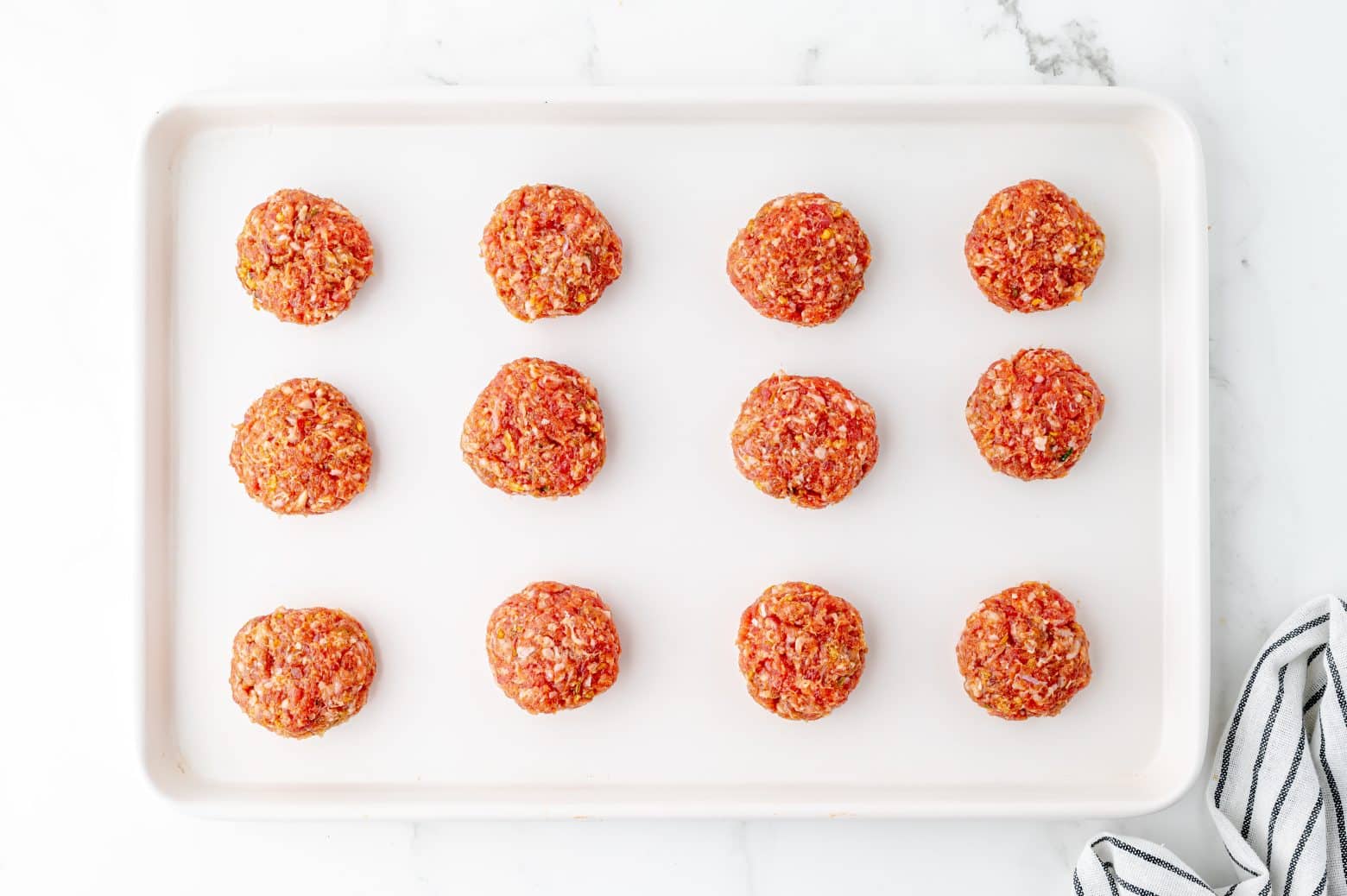 formed sausage slider patties on a white rimmed baking sheet