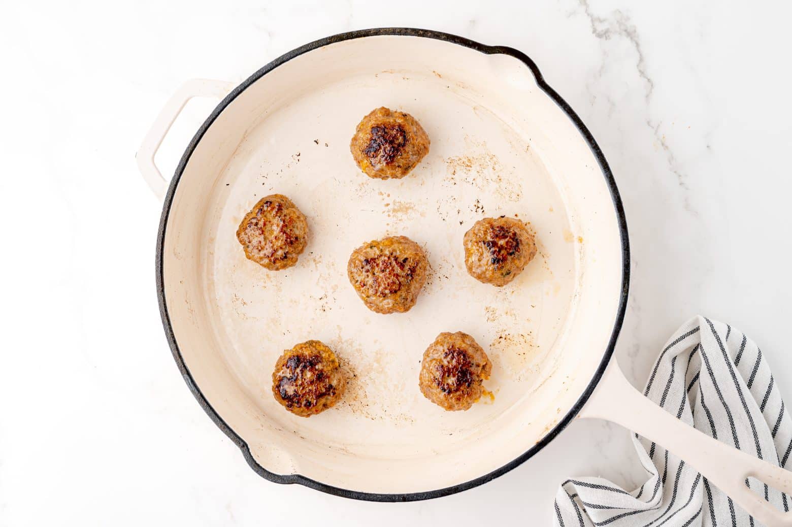 browning sausage patties in a white cast iron skillet