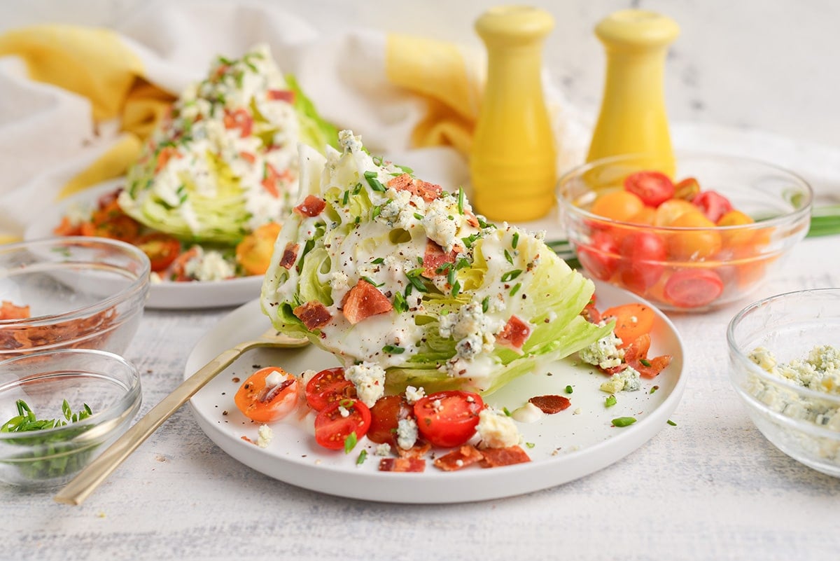 straight on shot of wedge salad on plate with fork and tomatoes