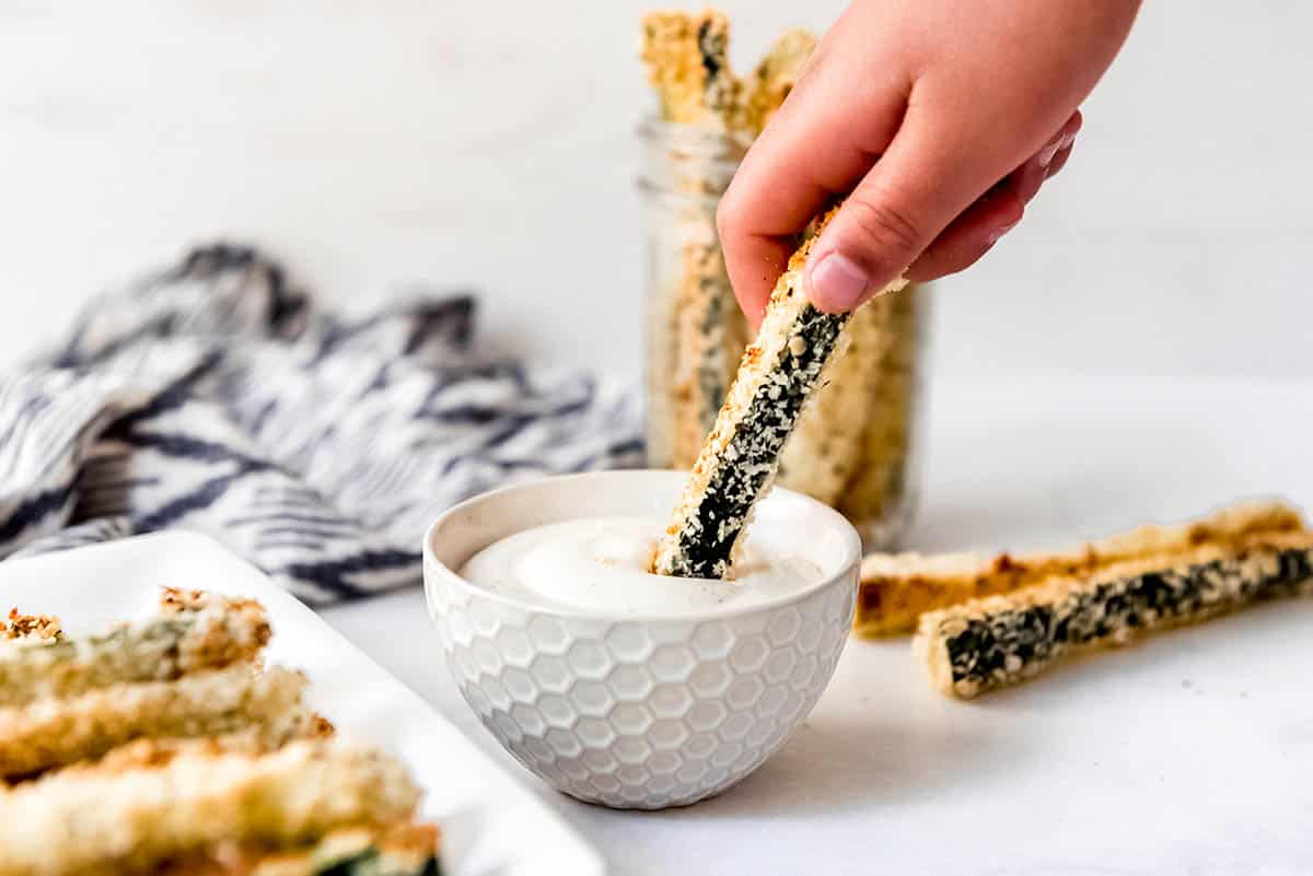 hand dipping zucchini fry in sauce