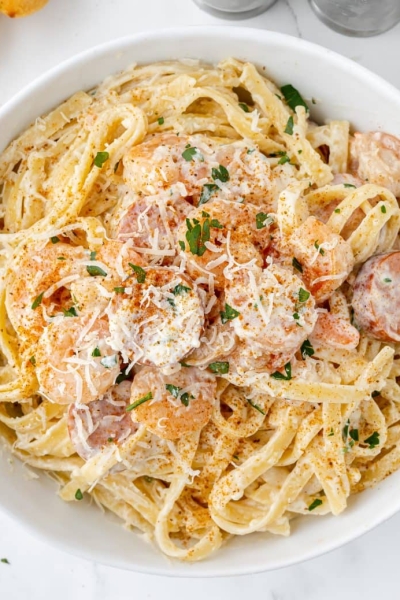 cajun shrimp alfredo in a white serving bowl with seasoning and shredded cheese