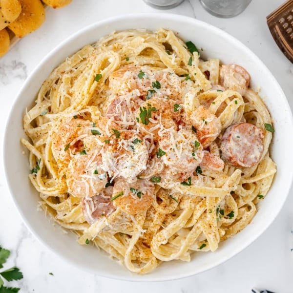 cajun shrimp alfredo in a white serving bowl with seasoning and shredded cheese