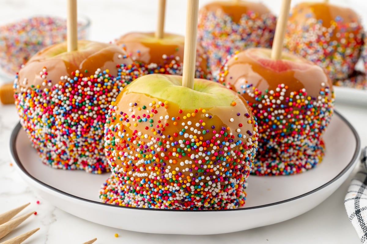 four caramel apples on a plate