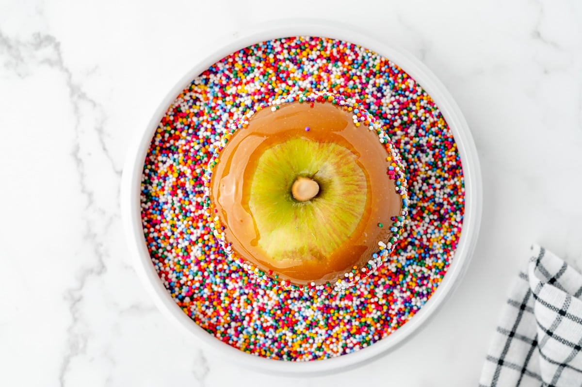 caramel apple dipping in sprinkles