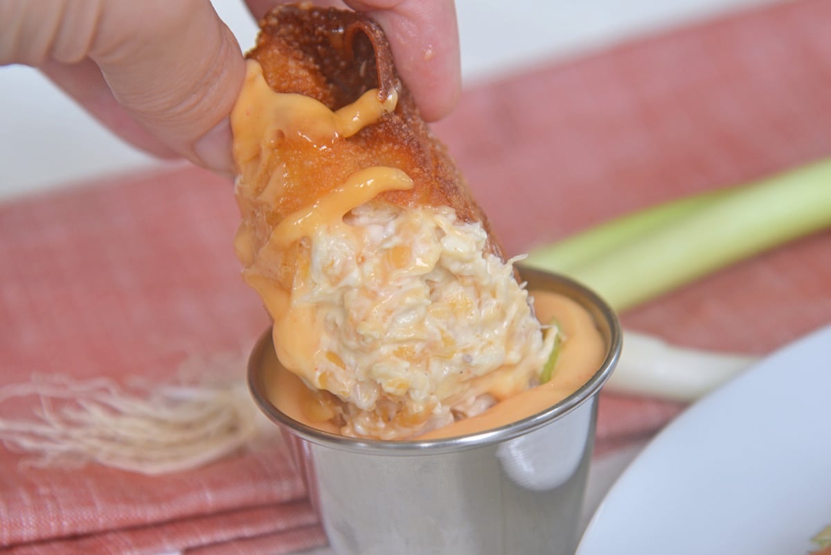 hand dipping egg roll in sauce