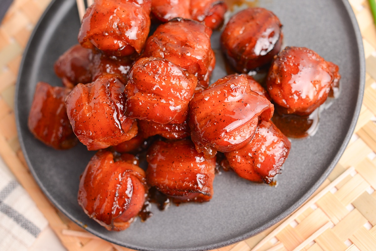 angled close up shot of brown sugar bacon wrapped kielbasa bites on a plate