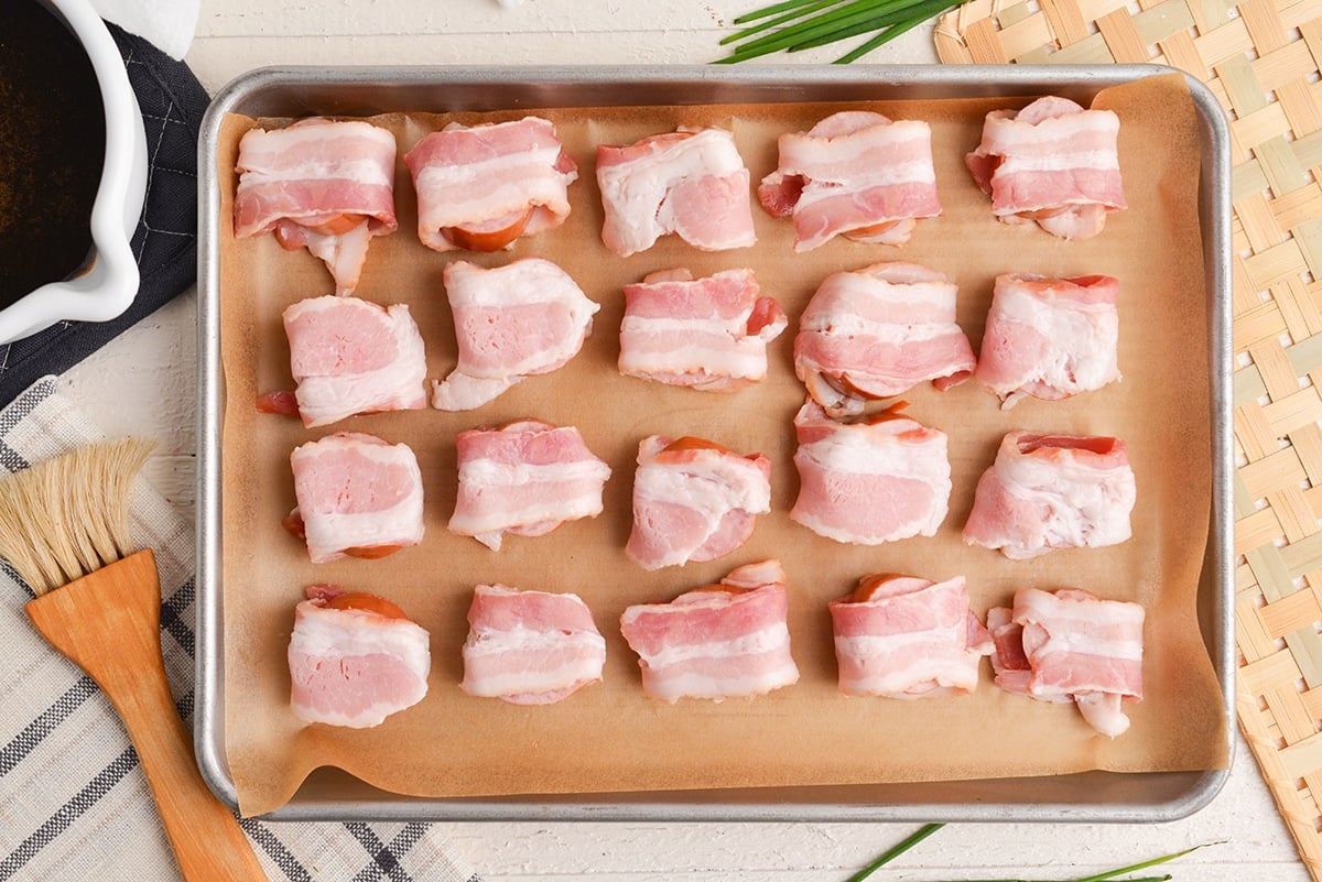 overhead shot of kielbasa wrapped in bacon on a sheet pan