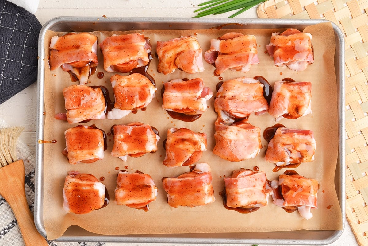 overhead shot of kielbasa wrapped in bacon and topped with brown sugar sauce on a sheet pan