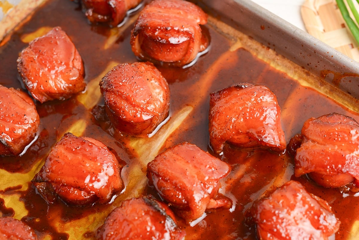 close up angled shot of brown sugar bacon wrapped kielbasa bites on a pan