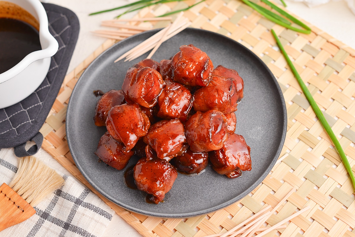 angled shot of plate of brown sugar bacon wrapped kielbasa bites on a plate