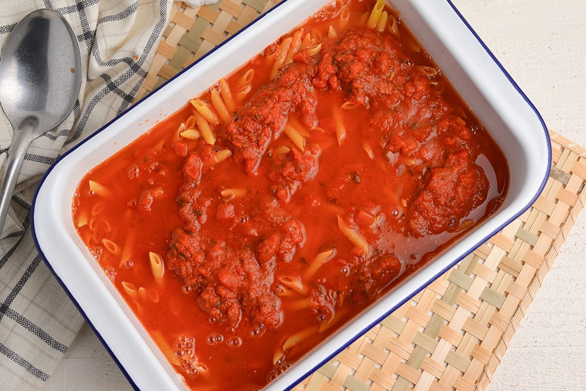 pasta sauce and water with dry pasta in a baking dish