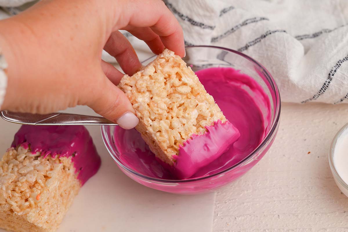 hand dipping rice krispie treat in melted chocolate