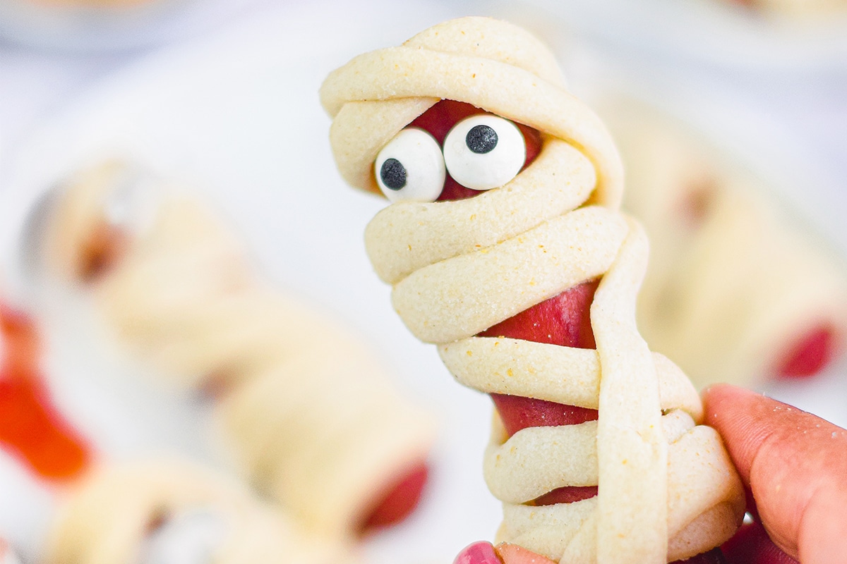 close up of hand holding mummy hot dog