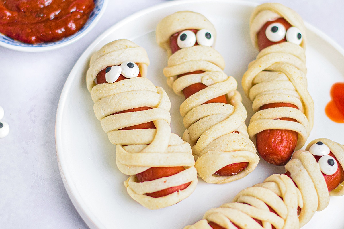 close up of four mummy hot dogs on plate