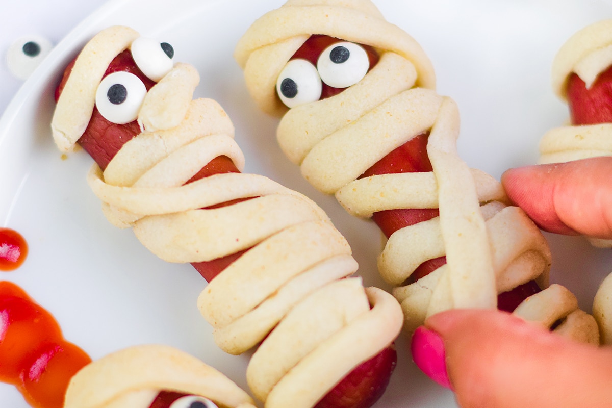 hand grabbing mummy hot dog from plate