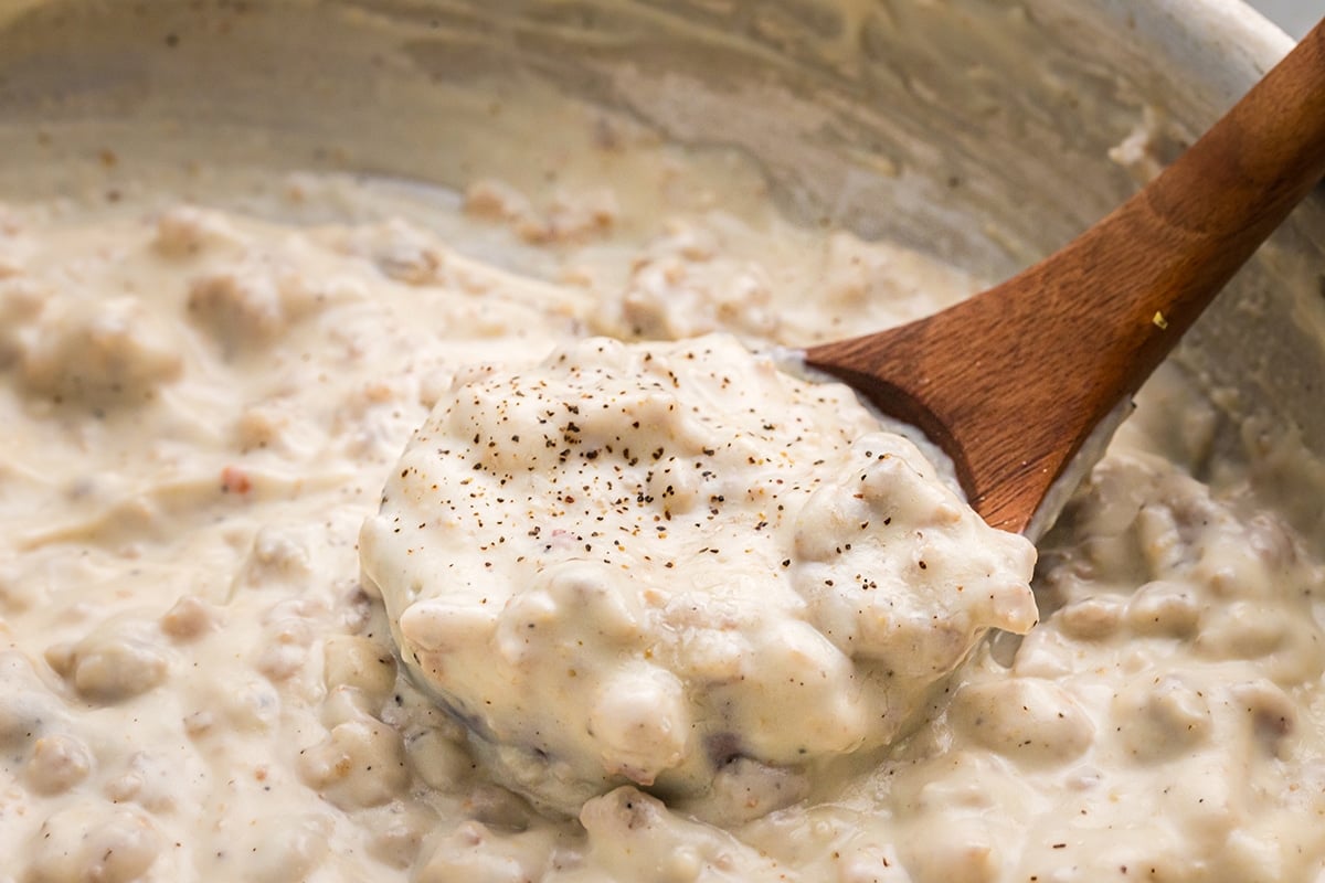close up angled shot of wooden spoon in pan of sausage gravy
