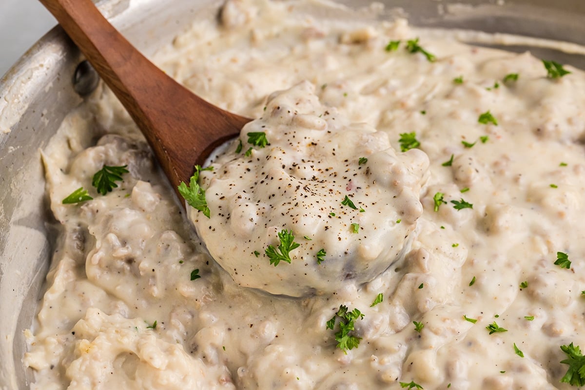 angled shot of wooden spoon in pan on creamy sausage gravy
